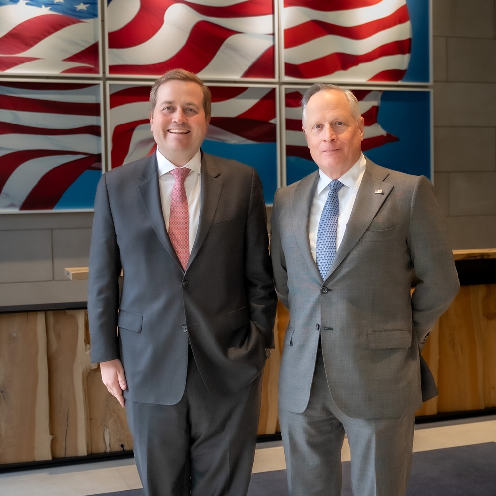 Hill and Ross Perot Jr. Standing in front of photographs of an American flag
